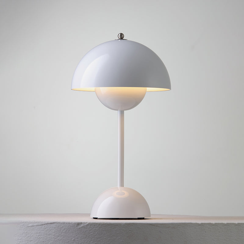 A white Clérachic table lamp lit, with a warm glow below the shade, on a pale stone ledge.