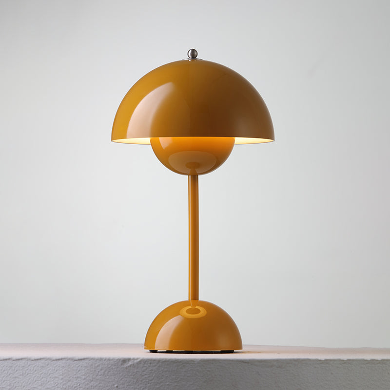 A mustard Clérachic table lamp lit, with a warm glow below the shade and a ring on the base, on a pale ledge.