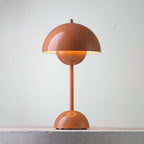A terracotta Clérachic table lamp lit, with a warm glow below the shade and a ring on the base, on a pale ledge.