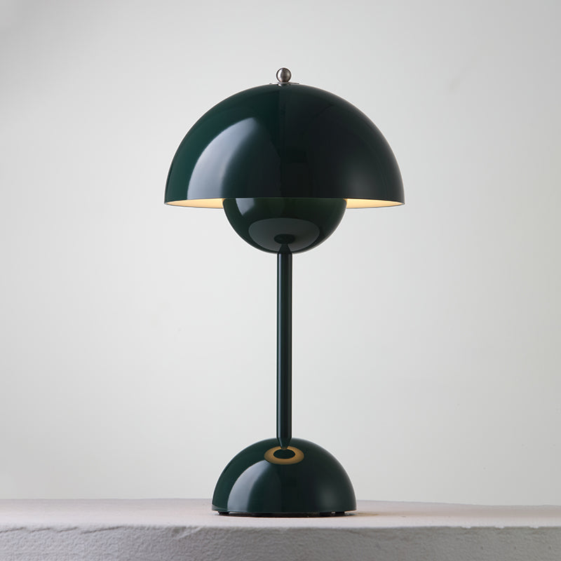 A dark-green Clérachic table lamp lit, with a bright rim under the shade and a ring on its base, on a pale ledge.