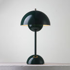 A dark-green Clérachic table lamp lit, with a bright rim under the shade and a ring on its base, on a pale ledge.