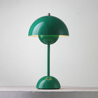 A green Clérachic table lamp lit, with a bright rim under the shade and a ring on its base, on a pale ledge.