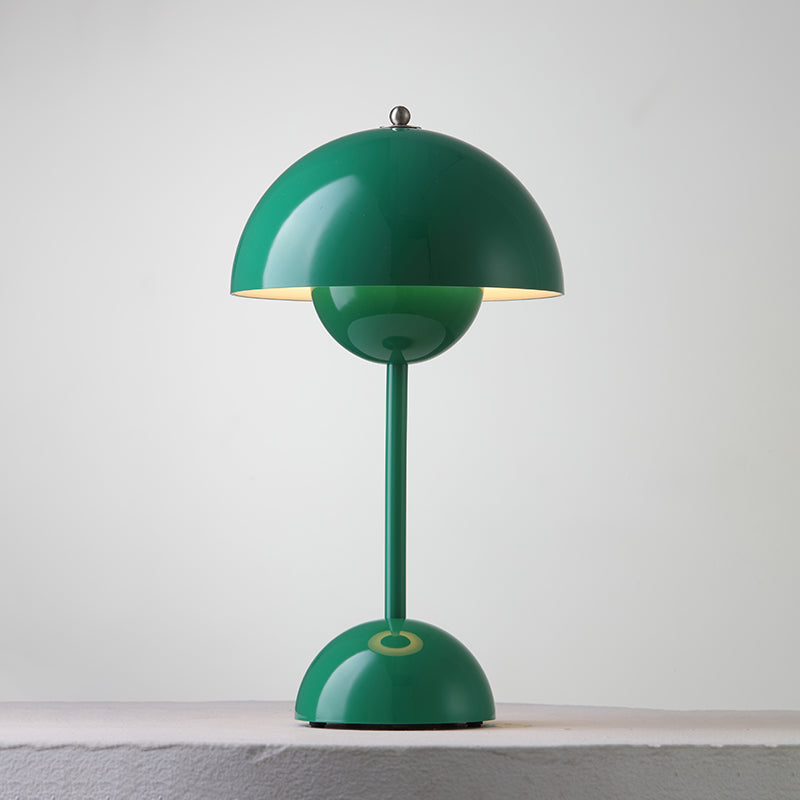 A green Clérachic table lamp lit, with a bright rim under the shade and a ring on its base, on a pale ledge.