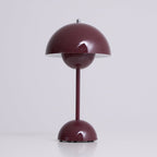 Three-quarter view of this Clérachic table lamp in deep plum, lit, with a bright rim under the dome, on a pale grey ground.