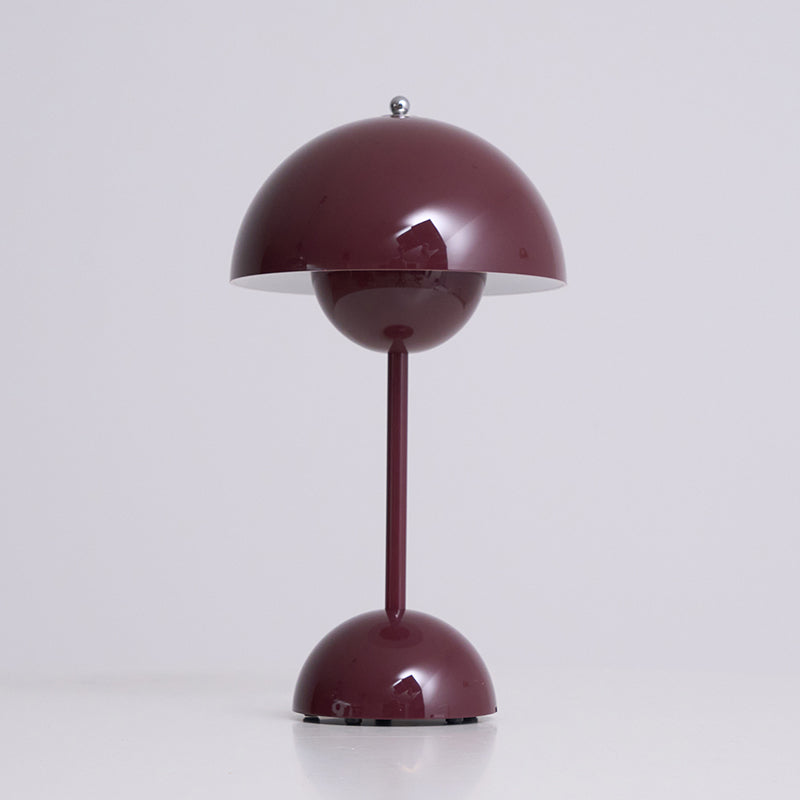 Three-quarter view of this Clérachic table lamp in deep plum, lit, with a bright rim under the dome, on a pale grey ground.