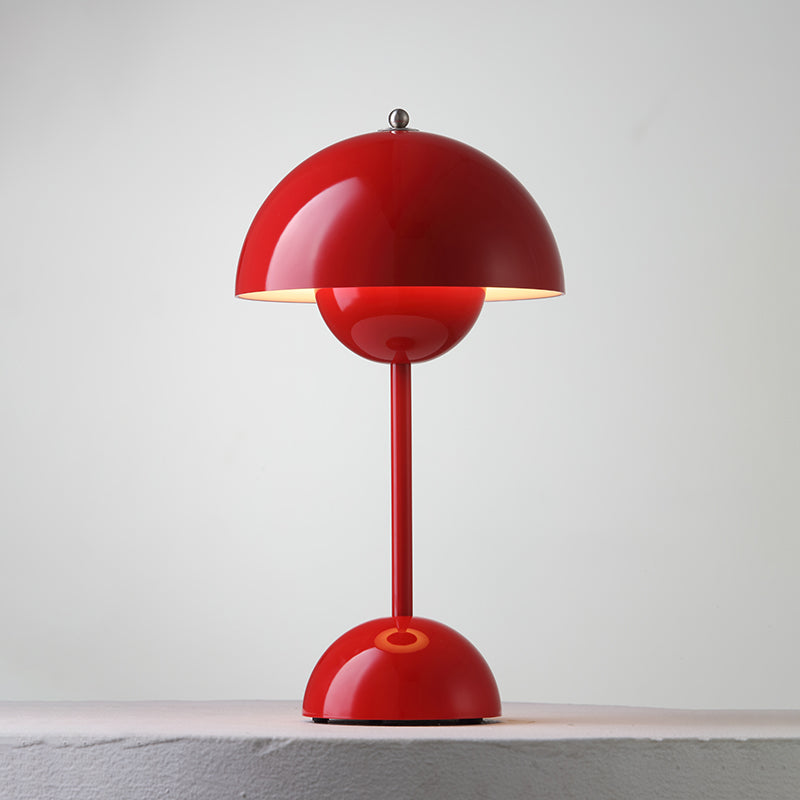 A red Clérachic table lamp lit, with a bright rim under the shade and a ring on its base, on a pale ledge.