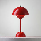 A red Clérachic table lamp lit, with a bright rim under the shade and a ring on its base, on a pale ledge.