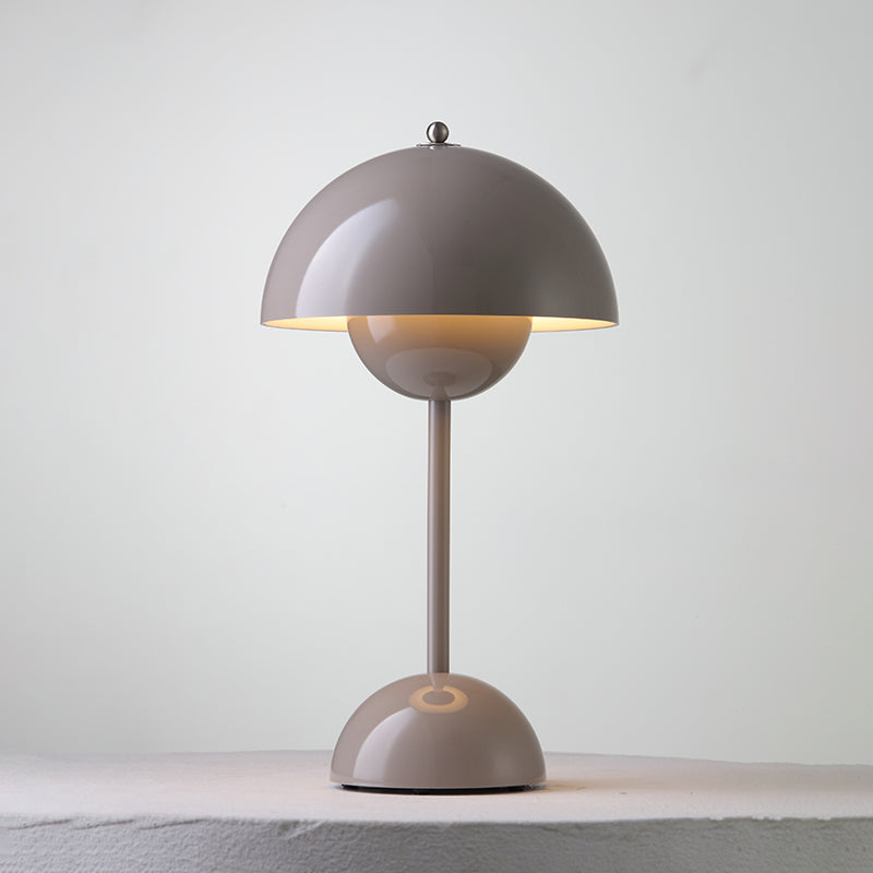 A taupe-grey Clérachic table lamp lit, with a warm glow under the shade and a ring on its base, on a pale ledge.