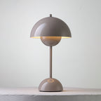 A taupe-grey Clérachic table lamp lit, with a warm glow under the shade and a ring on its base, on a pale ledge.