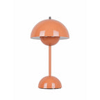 An orange Clérachic table lamp lit, with a glossy dome shade and a rounded base, on a plain white backdrop.