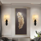 Pair of Clérachic wall lights with black columns and lit linen shades, flanking a large gold feather artwork on a panelled wall.
