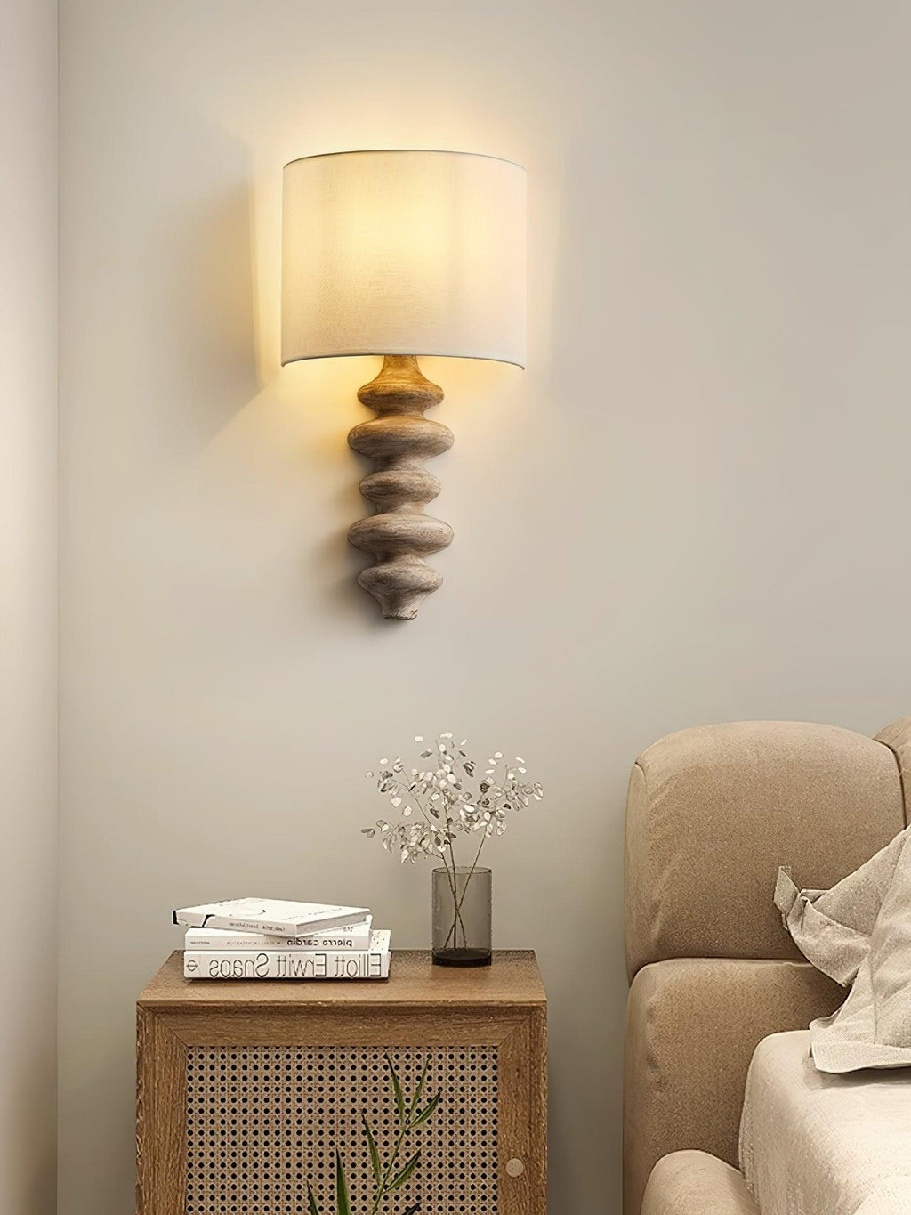 Clérachic wall light with a natural wood column and a white shade, above a rattan bedside cabinet and a cream sofa.