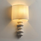 Lit Clérachic wall light with a white column, light spreading up and down the wall from its linen shade.