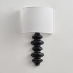Clérachic wall light switched off, with a white linen shade over a black corrugated wooden column on a light wall.