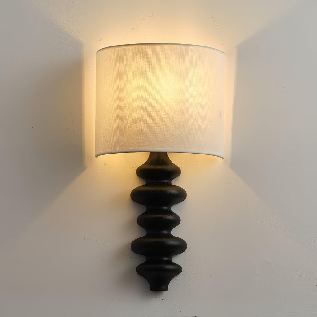 Lit Clérachic wall light with a glossy black corrugated column and a white shade, seen straight on against a light wall.