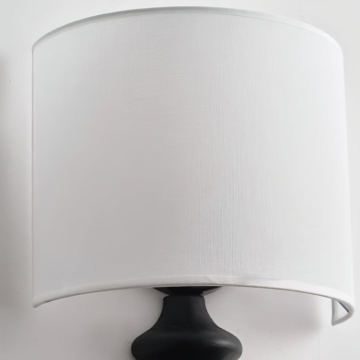 Close view of the fine white linen weave on the shade of this Clérachic wall light, above the top of its black column.