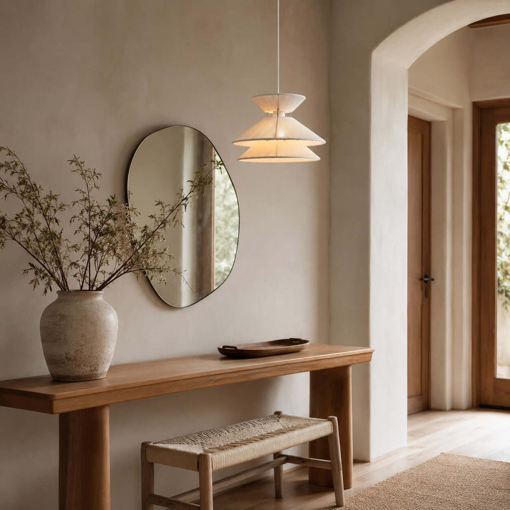 This Clérachic pendant light hangs by an arched doorway, beside an oval mirror and a wooden console with a woven stool.