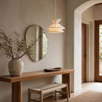 This Clérachic pendant light hangs by an arched doorway, beside an oval mirror and a wooden console with a woven stool.