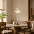 A tiered Clérachic pendant light lit over a round stone-topped table with wooden chairs and a cushioned corner seat.