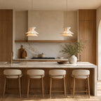 Two Clérachic pendant lights hang side by side above a marble-topped island with four cushioned wooden stools.
