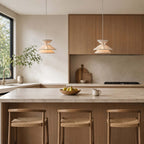 Two tiered Clérachic pendant lights in a kitchen with oak cabinets, above an island with three woven-seat stools.
