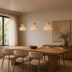 Three Clérachic pendant lights hang in a row above a long oak dining table with cream upholstered chairs.