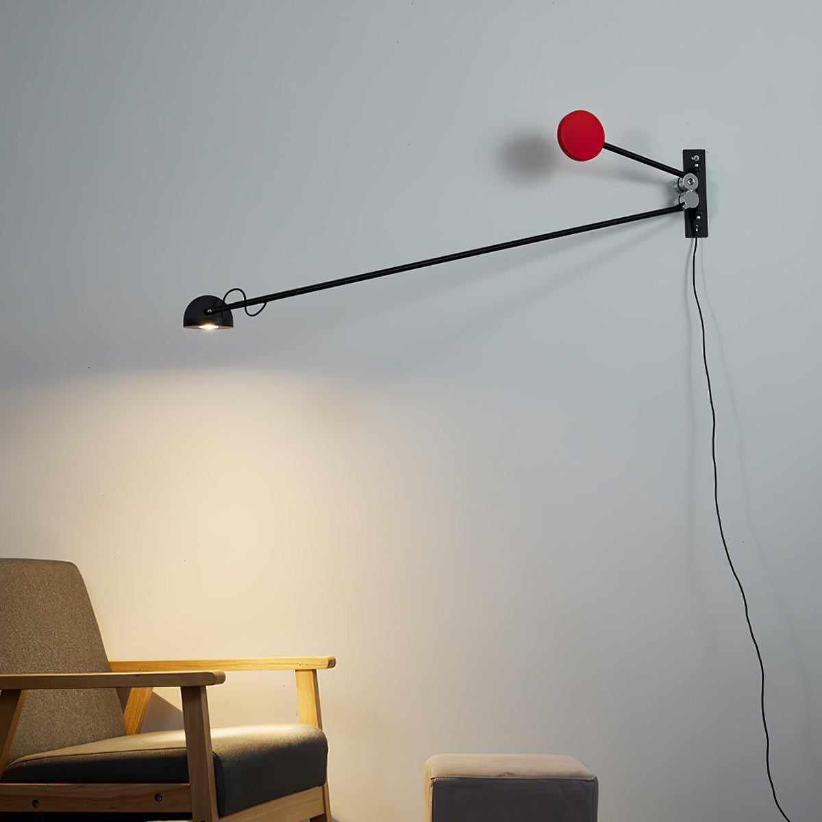 Black and red Clérachic wall light on a pale grey wall, its lamp head casting a soft pool of light above a wooden armchair.