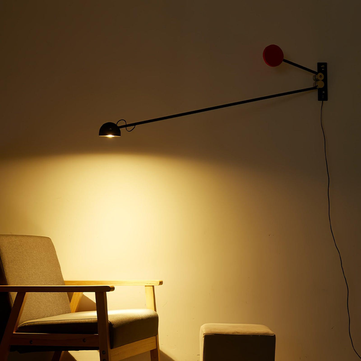 Warm amber glow spreads across the wall beneath this Clérachic arm light, with the red counterweight and a wooden armchair below.