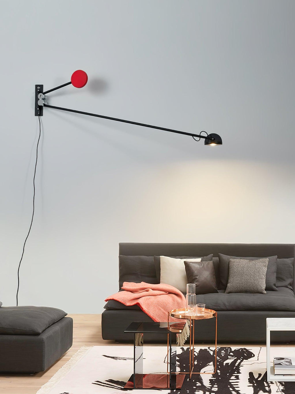 Clérachic wall light with its arm swung to the right, red counterweight at the back, above a dark grey sofa and a copper side table.