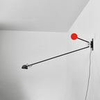 Clérachic arm light in a white corner, a long black arm stretching away from the wall with a red counterweight disc beside the mount.