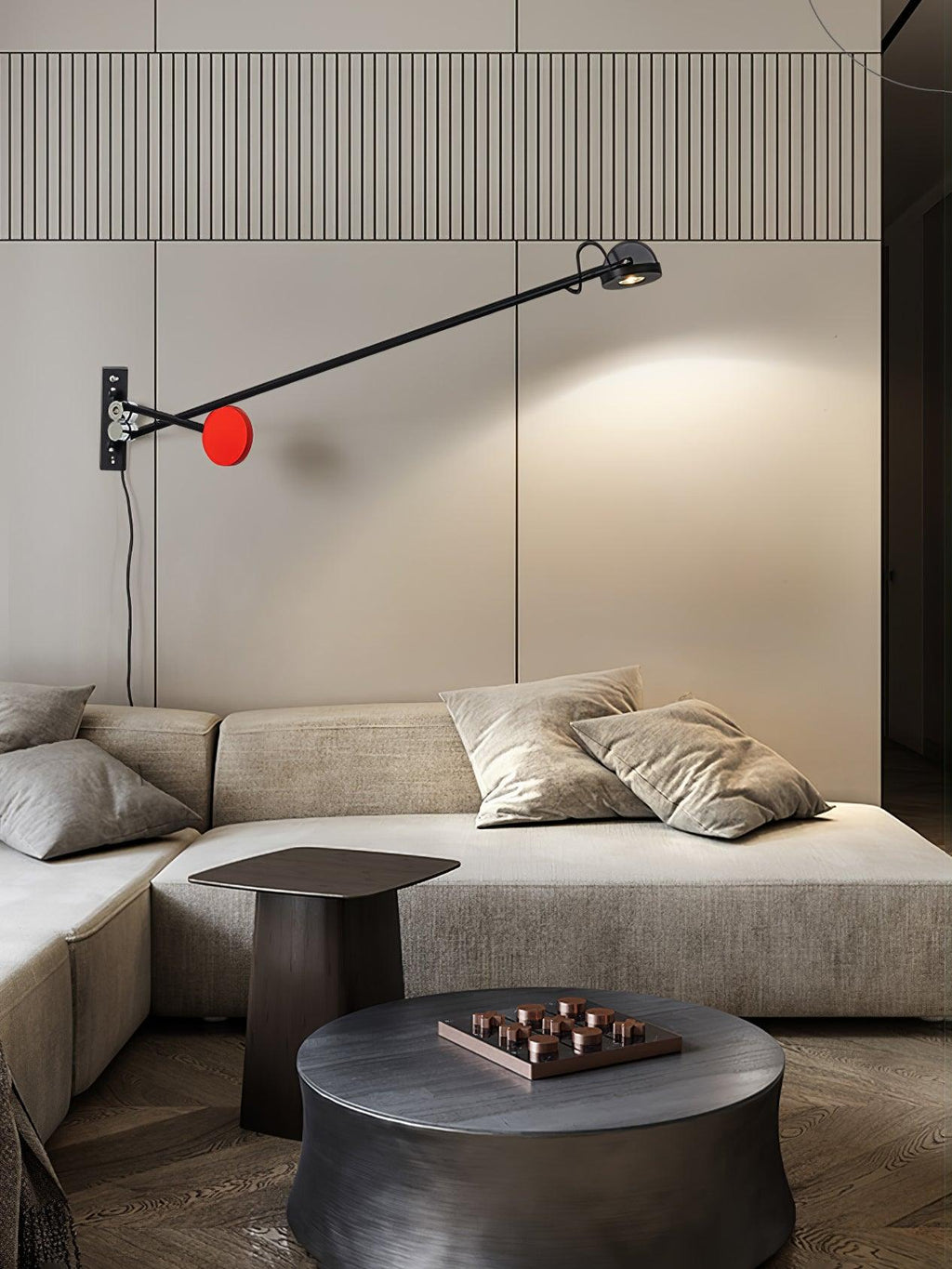 Clérachic wall light with a red counterweight above a stone-coloured corner sofa and a dark round coffee table, its arm reaching to the right.