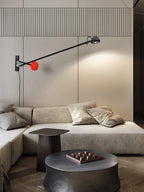 Clérachic wall light with a red counterweight above a stone-coloured corner sofa and a dark round coffee table, its arm reaching to the right.