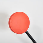 Close view of the round red counterweight disc and black arm on this Clérachic wall light, against a pale backdrop.