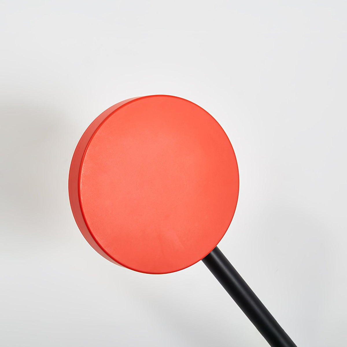 Close view of the round red counterweight disc and black arm on this Clérachic wall light, against a pale backdrop.
