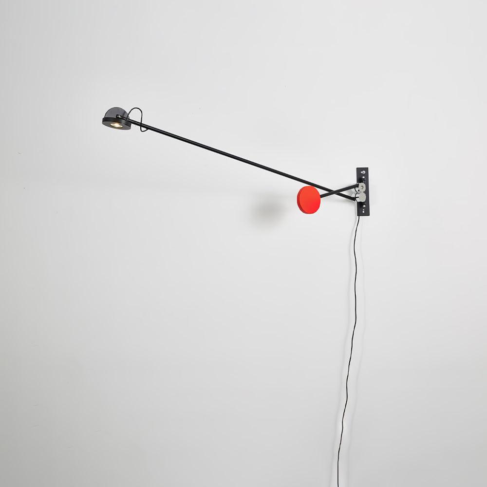Clérachic wall light on a pale wall with its arm swung left and level, the red counterweight tucked low beside the backplate.