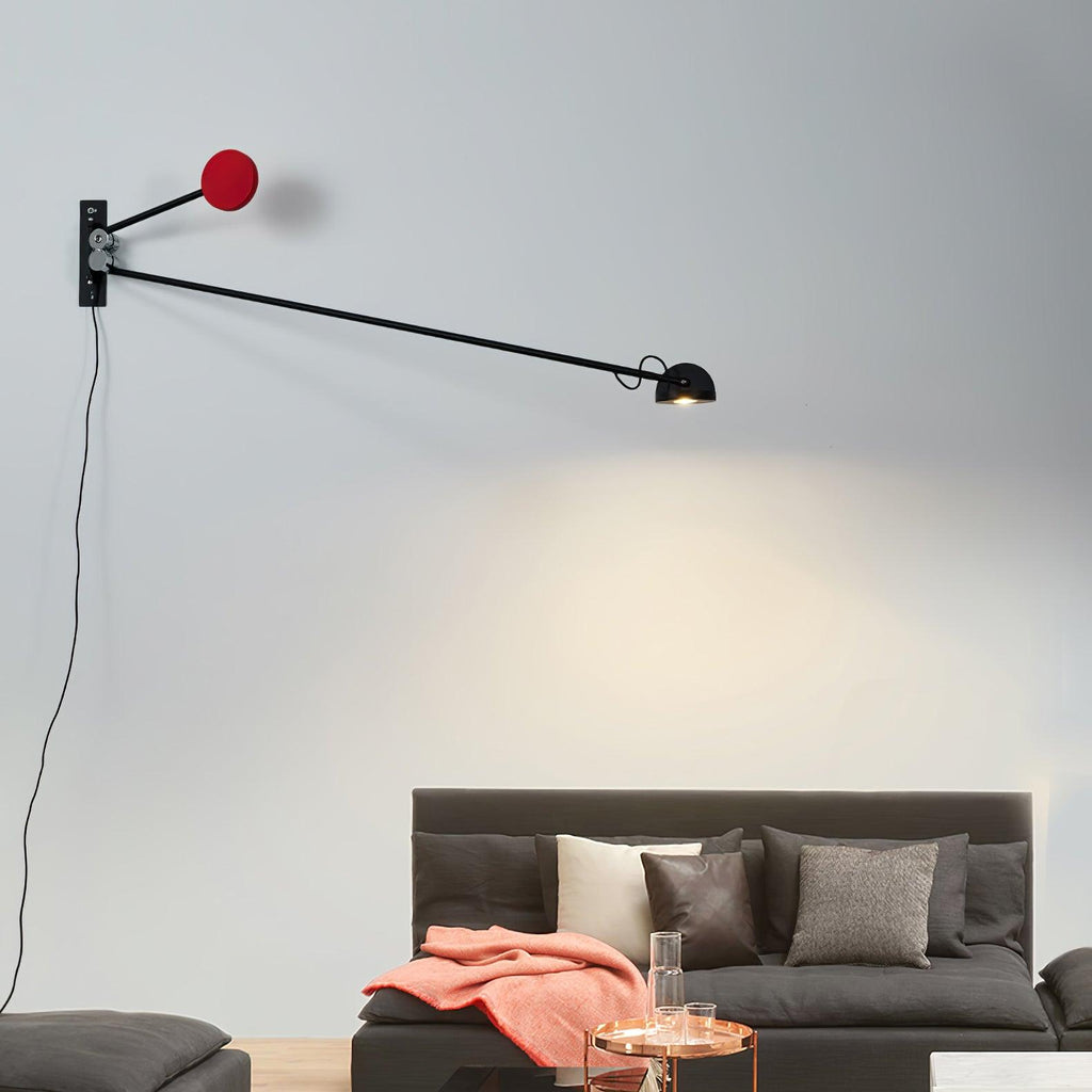 Black and red Clérachic wall light with a long level arm, its lamp head lighting the wall above a charcoal sofa with a coral throw.