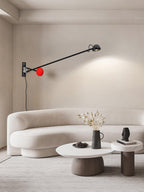 Clérachic wall light with a red counterweight low by the mount, its arm reaching right above a curved cream sofa and round white tables.
