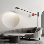 This Clérachic arm light on a warm white wall, the red counterweight beside the mount, above a ribbed grey sofa and a round coffee table.