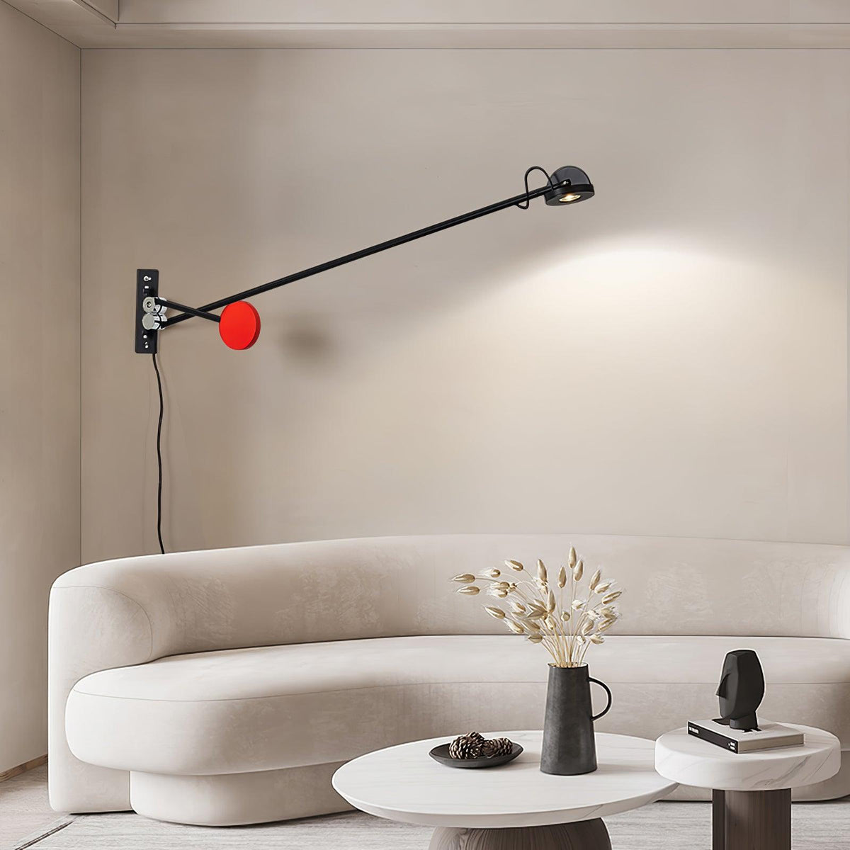 Clérachic wall light with a red counterweight, its lamp head throwing a soft arc of light above a curved cream sofa and a small vase.