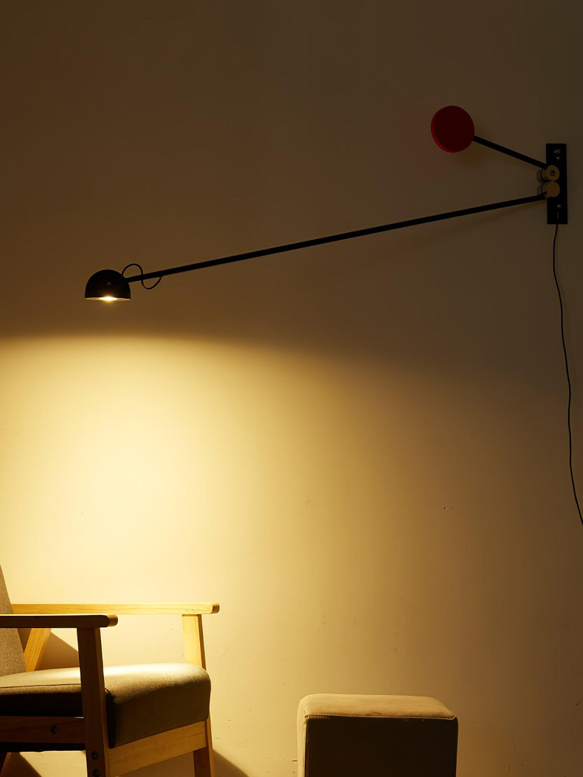A dim, amber-toned room with this Clérachic wall light switched on, the red counterweight above and a wooden armchair in the glow.