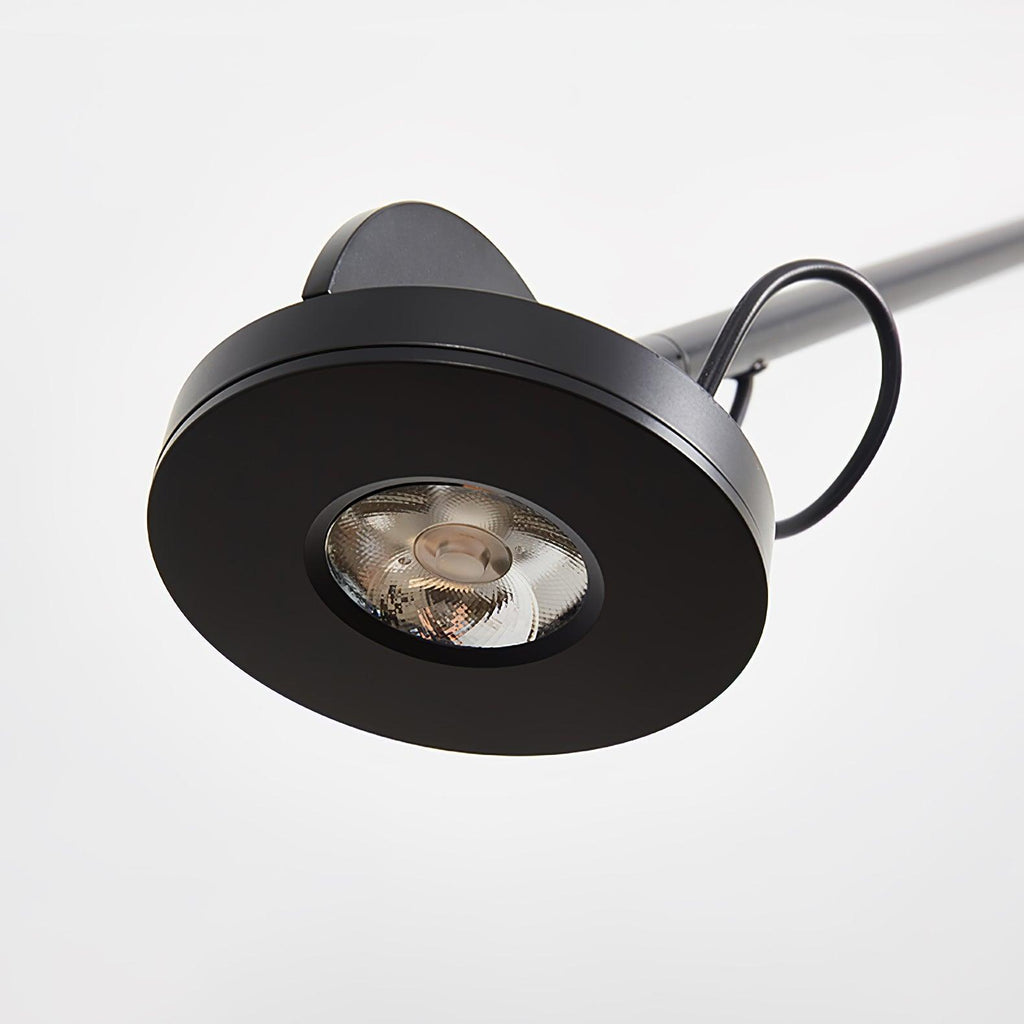 Close view of the round black lamp head on this Clérachic wall light, with its recessed light source and a loop of cable.