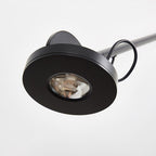 Close view of the round black lamp head on this Clérachic wall light, with its recessed light source and a loop of cable.