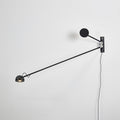All-black Clérachic wall light on a white wall, the arm reaching down to the left from a black disc counterweight.