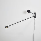 All-black Clérachic wall light on a white wall, the arm reaching down to the left from a black disc counterweight.