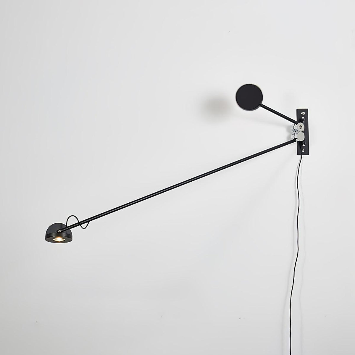 All-black Clérachic wall light on a white wall, the arm reaching down to the left from a black disc counterweight.