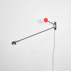 Black and red Clérachic wall light on a white wall, its long arm angled down to the left with the red counterweight above the mount.