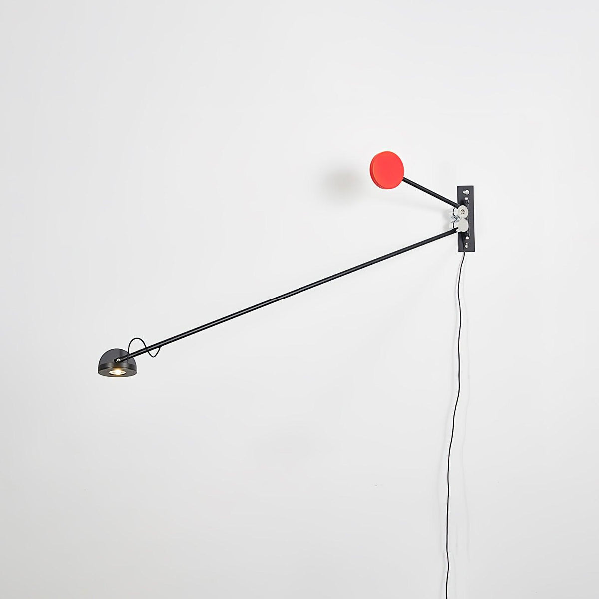 Black and red Clérachic wall light on a white wall, its long arm angled down to the left with the red counterweight above the mount.