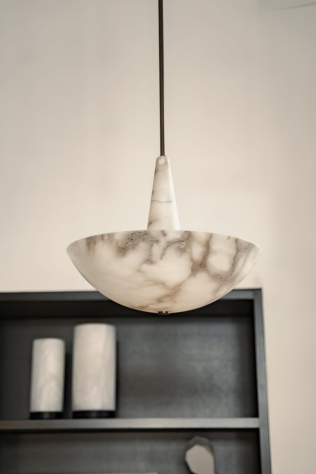 A pale grey-veined Clérachic Cove alabaster pendant against a cream wall above a dark shelf, showing the stone's natural markings