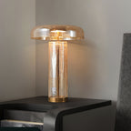 A Clérachic amber crackle-glass table lamp glowing on a dark bedside unit, its domed shade above a clear cylindrical body.