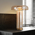 This Clérachic crackle-glass table lamp stands on a dark wood sideboard beside a window with slatted blinds, lit warm.